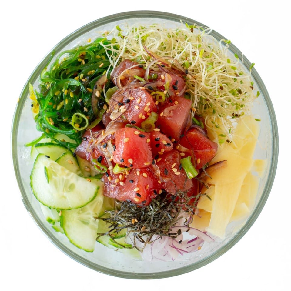 Overhead view of a POKÉ + GO poke bowl with tuna, seaweed, cucumber, sprouts, and ginger.