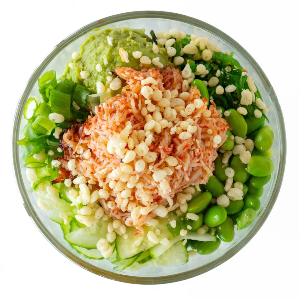 Overhead view of a POKÉ + GO poke bowl with crab, avocado, edamame, and crispy toppings.