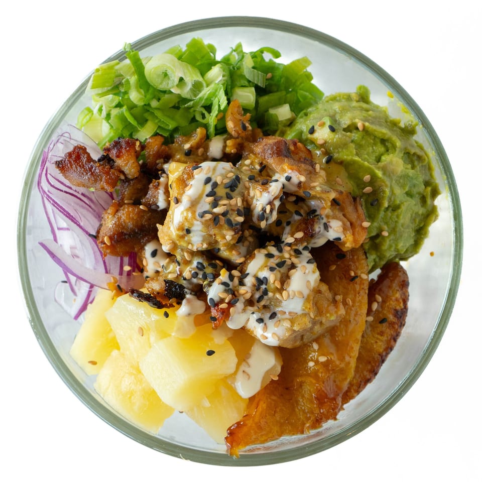 Top-down view of a POKÉ + GO poke bowl with chicken, guacamole, pineapple, and green onions.